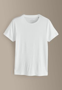 Jednoduché biele tričko s krátkym rukávom a okrúhlym výstrihom, strednej veľkosti, vystavené na béžovom pozadí.