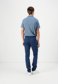 Polo bleu à manches courtes avec un motif texturé, associé à un pantalon slim-fit bleu marine et des baskets blanches. Pas de logos ni d'accents visibles.
