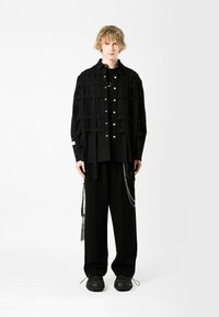 Camisa negra de capas con cierre de botones, que presenta una textura en forma de cuadrícula. Combinada con pantalones negros holgados y zapatos negros texturizados.