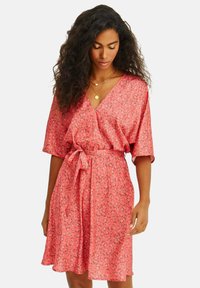 Korálové květinové šaty s V-výstřihem, krátkými rukávy a páskem v pase. Vyrobené z lehké tkaniny s jemnou texturou a malými, nenápadnými květinovými vzory.