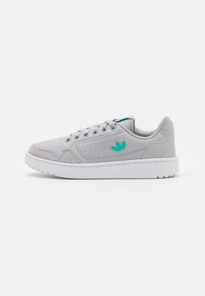 Baskets Adidas gris clair avec logo bleu sarcelle sur le côté, sept œillets pour les lacets, détails perforés et semelle blanche, vues de profil.