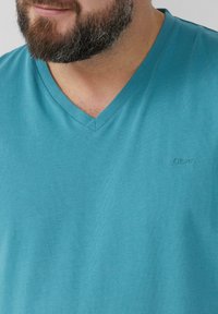 Een zachte, turquoise V-hals t-shirt met een gestructureerde stof. Heeft een subtiel logo in de bovenste linkerhoek. Ideaal voor casual kleding.