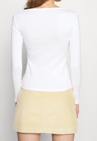 Long-sleeved white top with a rounded neckline, paired with a light yellow corduroy skirt featuring vertical ribbed texture.