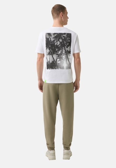 Hvid t-shirt med et sort palmetræ grafik på ryggen, parret med olivengrønne joggers og lyse sneakers.