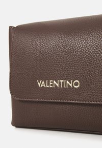 Rjav usnjen denarnica z zlatim logotipom "Valentino". Ima preklopno zapiranje in vidne šive.