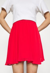 Jupe rouge longueur genou avec une ceinture élastique et un tissu léger et fluide. Associée à un t-shirt blanc court.