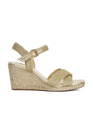 Sandale à semelle compensée avec une bande tissée dorée et une semelle en jute naturel texturée. Elle dispose d'une sangle réglable avec une boucle dorée et d'une zone de orteil brillante.