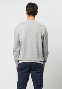 Un hanorac gri cu mâneci lungi, cu măneci din bumbac, și guler rotund, purtat cu pantaloni bleumarin. Textură moale, design simplu, fără modele vizibile.
