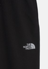 Svarta fleece byxor med vit broderad logotyp av The North Face på nedre vänstra sidan. Mjukt material, elastisk midja.