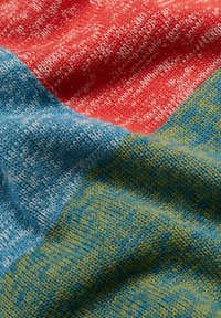Mehrfarbiger Strickstoff mit roten, blauen und grünen Abschnitten und einem strukturierten Muster. Das Garn wirkt weich und ist mit sichtbaren Stichen gewebt.