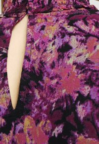 Tessuto a fiori viola con superficie testurizzata. Presenta un'apertura a chiave sul retro e dettagli di scollatura arricciata.