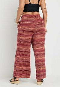 Breda byxor i ett texturerat tyg med ett zick-zack mönster i nyanser av röd och orange. Elastisk midjeband och sidfickor.