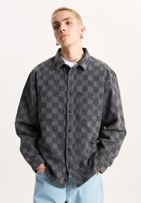 Grijze geruite denim overhemd, met twee voorkruiden en een button-down kraag. Lange mouwen, relaxte pasvorm, met lichtblauwe spijkerbroek.