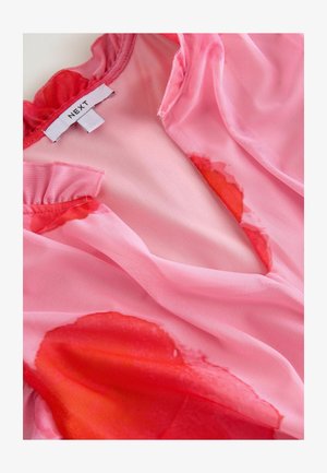 Blusa rosa transparente con cuello con volantes, que presenta un patrón floral rojo en estilo acuarela. Etiqueta visible con la marca "NEXT".