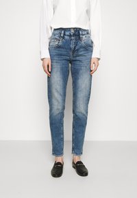 Calças de ganga azul claras com um design de perna reta, detalhes desbotados, estilo de cinco bolsos e fecho com botão, combinadas com mocassins pretos.