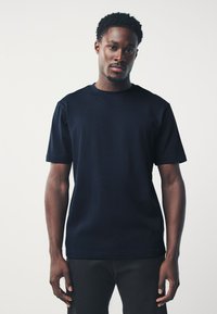 Camiseta de manga corta en azul marino hecha de algodón. Cuello redondo y ajuste relajado, con textura lisa y sin patrones o detalles visibles.