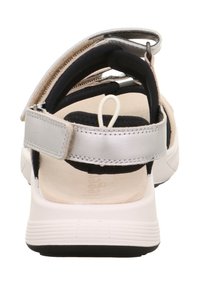 Tył sandała z regulowanymi czarnymi i srebrnymi paskami, miękką beżową wkładką i solidną białą podeszwą z czarnymi akcentami.