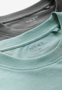 To sæt crew-neck t-shirts stablet; den ene i mørkegrå og den anden i lys mintgrøn. Begge har ribbede kraver og et mærke indvendigt.