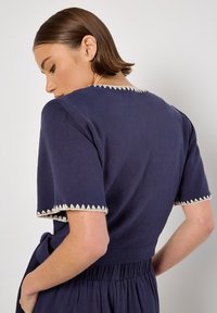 Navyblaues Baumwollkleid mit kurzen Ärmeln und dekorativem cremefarbenem Besatz. Das Kleid hat eine taillierte Taille und einen lockeren Rock.