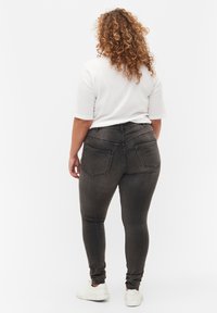 Jeans oscuros ajustados de cintura alta, con dos bolsillos traseros y una textura suave. Combinados con una camisa blanca holgada y zapatos blancos.