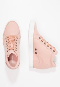 Růžové plátěné vysoké tenisky s bílou gumovou podrážkou. Mají šněrování a kovové průchodky, s logem na vnitřní části jazyka a na boku.