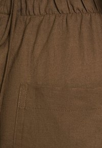 Tissu brun au toucher doux et texturé, avec une taille élastique et un détail de poche latérale.