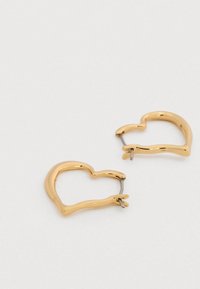 Σκουλαρίκια κρίκοι σε σχήμα καρδιάς με χρυσό τόνο, με λεία υφή και ανοιχτό σχέδιο, που διαθέτουν λεπτό μεταλλικό καρφί για κλείσιμο.