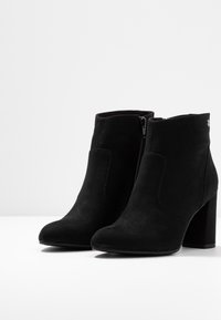 Botines de ante negro hasta el tobillo con puntera cerrada, featuring un zipper lateral y un tacón ancho. Textura suave y diseño minimalista.