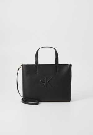 Borsa a tracolla in pelle nera con manici corti e una tracolla rimovibile. Caratterizzata dal logo "cK" in rilievo sul davanti. Texture liscia.