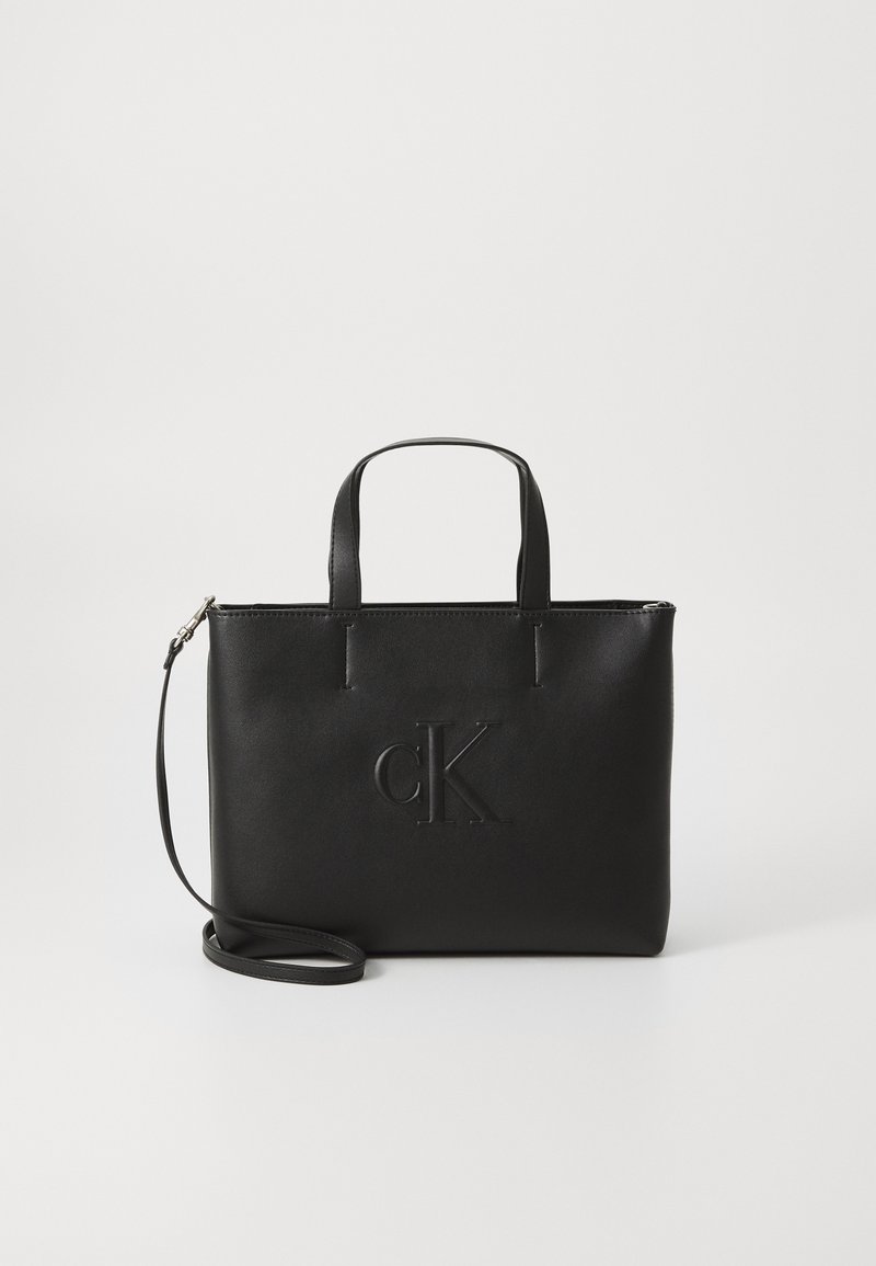 Czarna skórzana torba tote z krótkimi uchwytami i odpinanym paskiem na ramię. Posiada wytłoczone logo "cK" z przodu. Gładka faktura.
