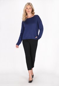 Pulover marin cu mâneci lungi și un croi lejer, asociat cu pantaloni negri scurți și pantofi cu toc înalt negri. Texturi netede pe tot parcursul.
