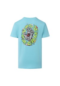 Camiseta de algodón azul claro con un estampado gráfico de una mano gris con la boca abierta, rodeada de acentos en verde y color en la parte posterior.