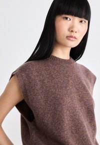 Brauner, ärmelloser Strickpullover aus strukturiertem Material, mit rundem Halsausschnitt und seitlichen Ausschnitten. Dezente lila Sprenkel durchgehend.