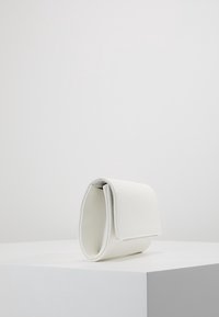 Borsa a mano in pelle bianca con design strutturato e arrotondato. Dispone di chiusura a patta e texture liscia. Posizionata su una superficie d'esposizione bianca.