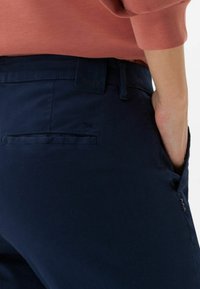 Námořnické modré kalhoty vyrobené z lehkého materiálu. Mají zadní kapsu, hladkou texturu a štítek s logem poblíž pasu.