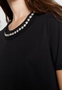 Svart t-shirt med en dekorerad halsringning med blommiga detaljer, korta ärmar och en mjuk bomullstextur.