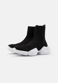 Botas tipo calcetín negras hasta el tobillo con una suela de goma blanca gruesa. Presentan un upper de punto suave y una tira en la parte posterior para facilitar ponerlas.