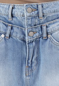 Jeans din denim albastru deschis, cu două butoane din metal, cusături vizibile și un design cu cinci buzunare. Materialul are o suprafață ușor texturată.