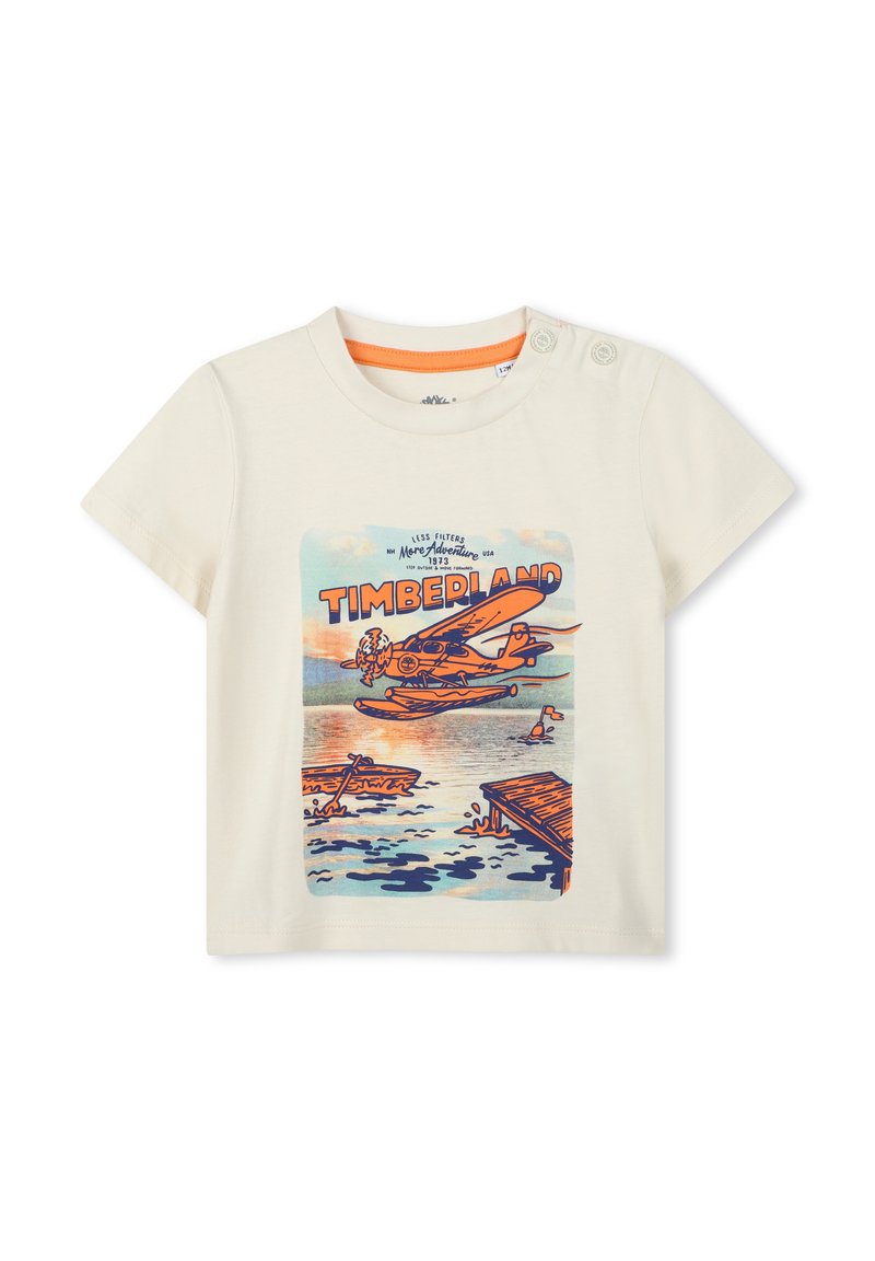 Korte mouw crèmekleurig t-shirt met een kleurrafgrafiek van een watervliegtuig en landschap, met oranje accenten rond de halslijn en knoopdetails.