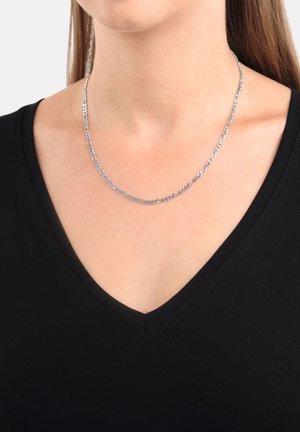 Collana in argento con maglie intrecciate, caratterizzata da una finitura liscia, indossata su un collo nudo, sopra una maglietta nera a V.