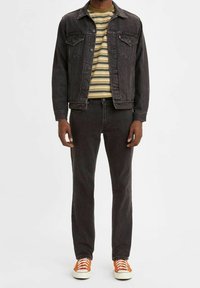 Černá džínová bunda, pruhované zeleno-žluté tričko, černé džíny a oranžové tenisky. Jednoduchý design, volný střih, klasické kovové detaily.