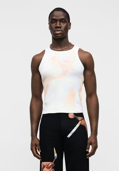 Άσπρο αμάνικο τοπ με ξεθωριασμένο γραφικό σχέδιο στο μπροστινό μέρος, συνδυασμένο με μαύρο παντελόνι που έχει έντονο εικονογραφημένο σχέδιο.