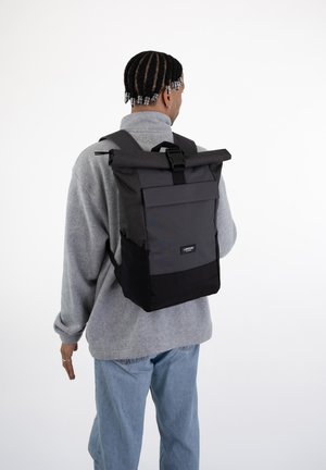 Black and gray roll-top backpack with adjustable straps, front pocket, and a sleek rectangular shape. Made of durable fabric.