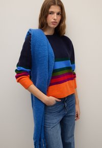 Colorful striped sweater in navy, orange, green, and purple with a cozy texture. Paired with a bright blue scarf, fringed at the ends.