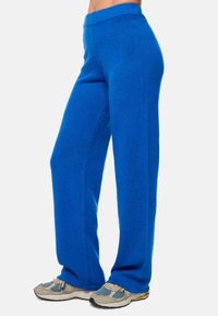 Pantalons de survêtement en polaire bleue avec une coupe décontractée, dotés d'une large taille, de jambes droites et d'une texture douce, associés à des baskets grises et bleues.