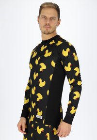 Black long-sleeve top featuring a pattern of yellow rubber ducks with red beaks. Material appears stretchy; sleek, modern fit.
