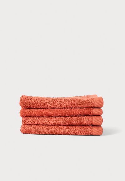 Quatre serviettes en éponge couleur corail soigneusement pliées, empilées sur un fond clair uni.