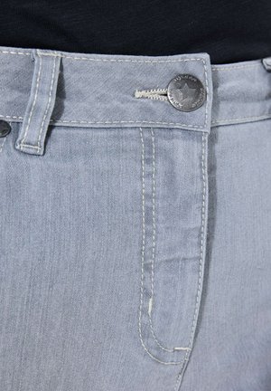 Makroaufnahme des hellblauen Jeansbunds mit Metallknopf, der einen Stern zeigt, und kontrastierender weißer Naht auf einem schwarzen Oberteil.