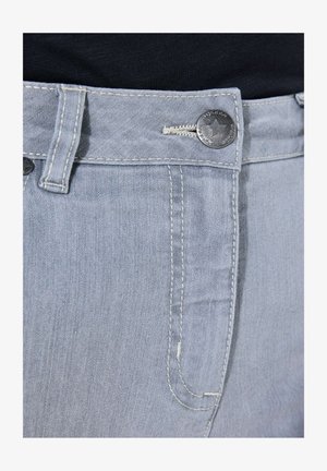 Makroaufnahme des hellblauen Jeansbunds mit Metallknopf, der einen Stern zeigt, und kontrastierender weißer Naht auf einem schwarzen Oberteil.