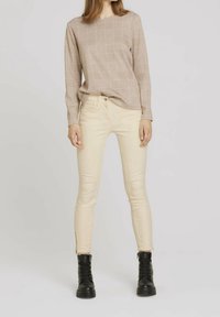 Top de manga larga de cuadros beige con escote cuadrado, combinado con jeans ceñidos crema con cremalleras laterales y botas negras con cordones.